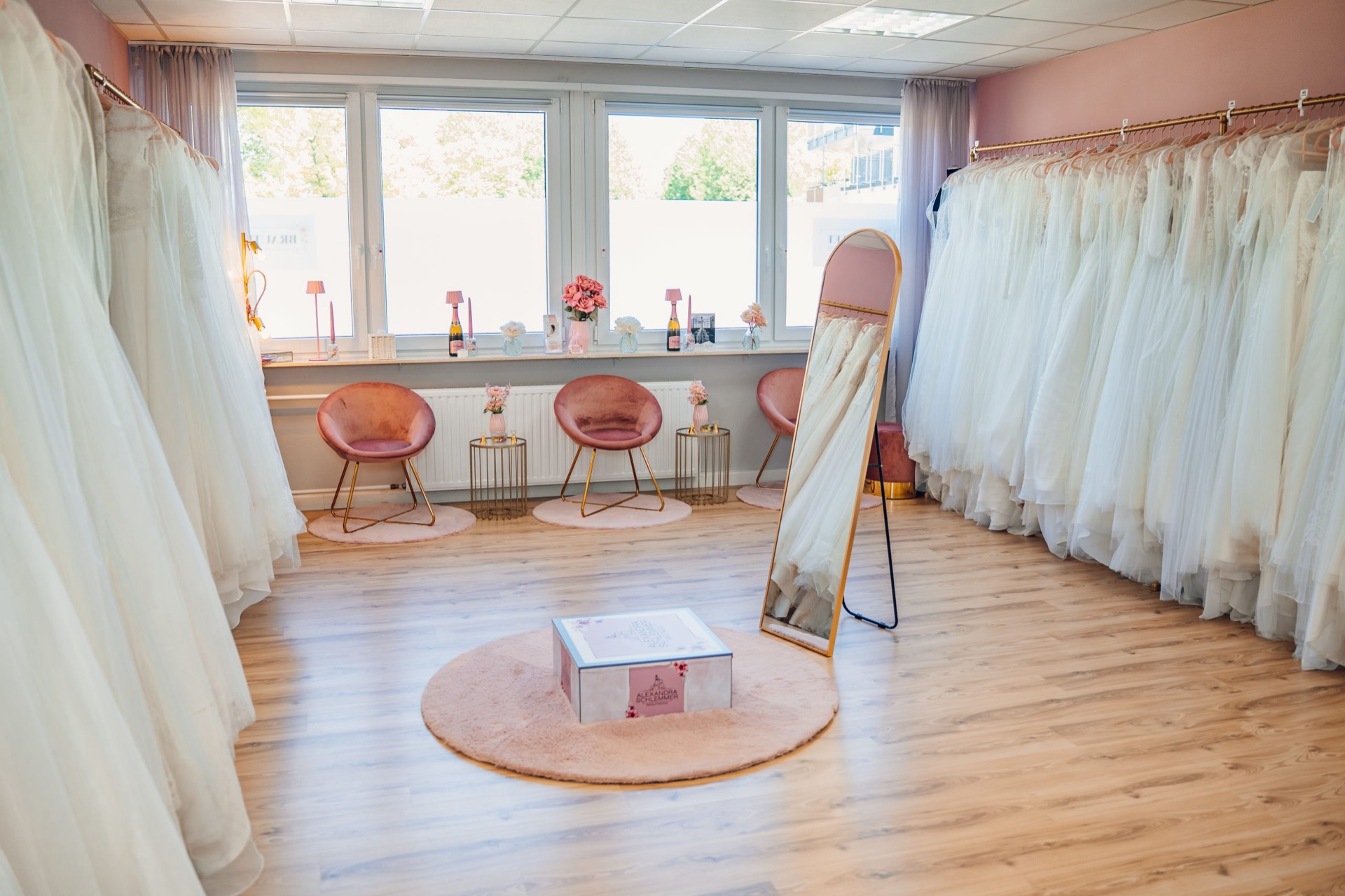 Der Showroom von Brautmode Saarpfalz: Brautkleider, rosa Samtsessel und goldener Spiegel